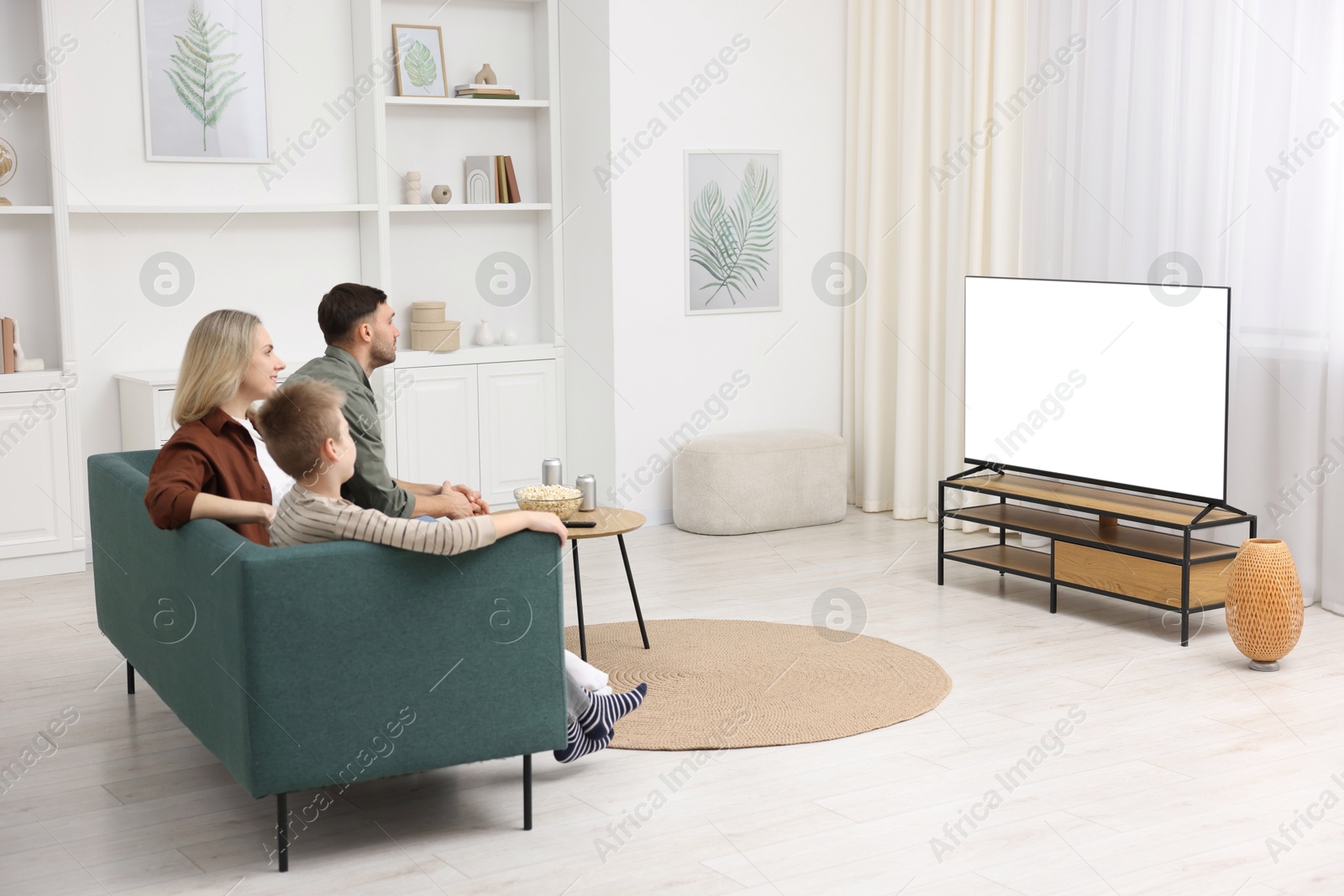 Photo of Happy family with snacks and drinks watching tv together at home