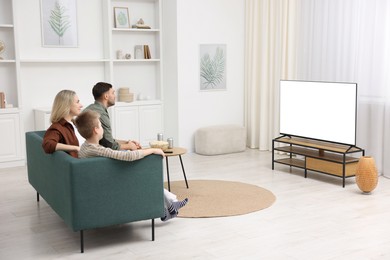 Photo of Happy family with snacks and drinks watching tv together at home