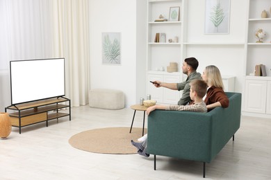 Photo of Happy family with snacks and drinks watching tv together at home