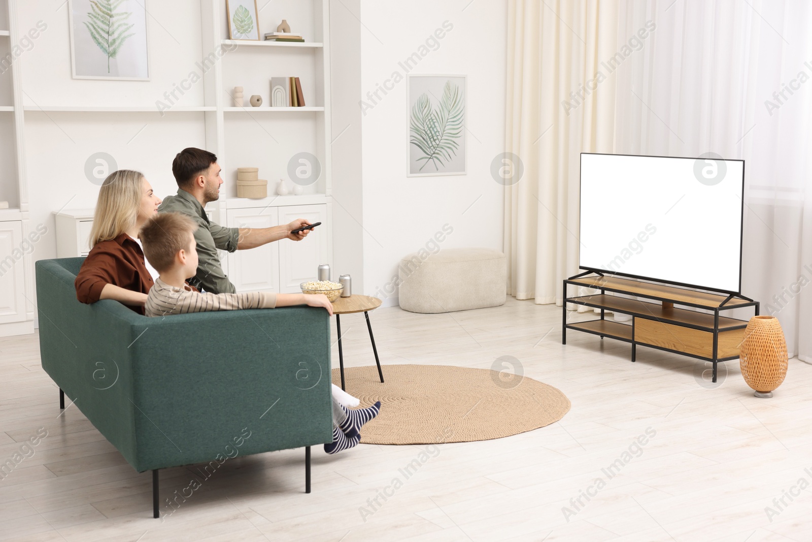 Photo of Happy family with snacks and drinks watching tv together at home