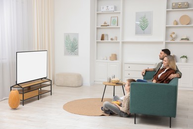 Photo of Happy family with snacks and drinks watching tv together at home