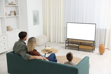 Photo of Happy family with snacks and drinks watching tv together at home