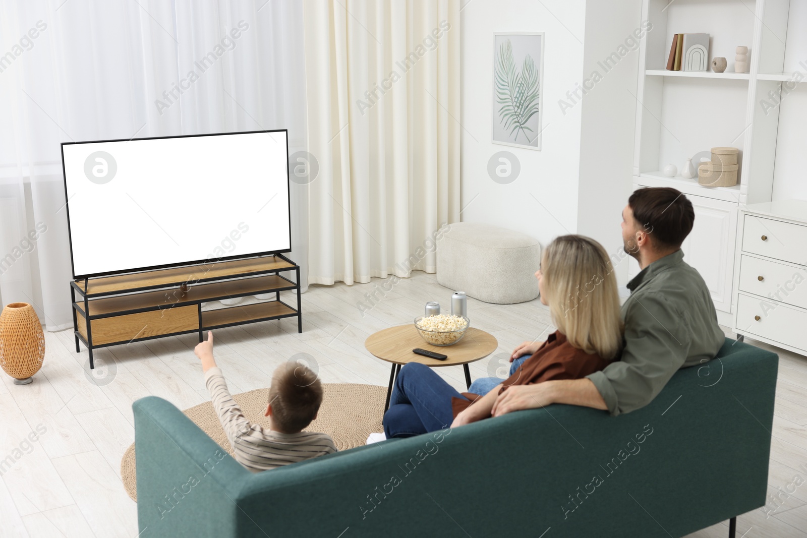 Photo of Happy family with snacks and drinks watching tv together at home