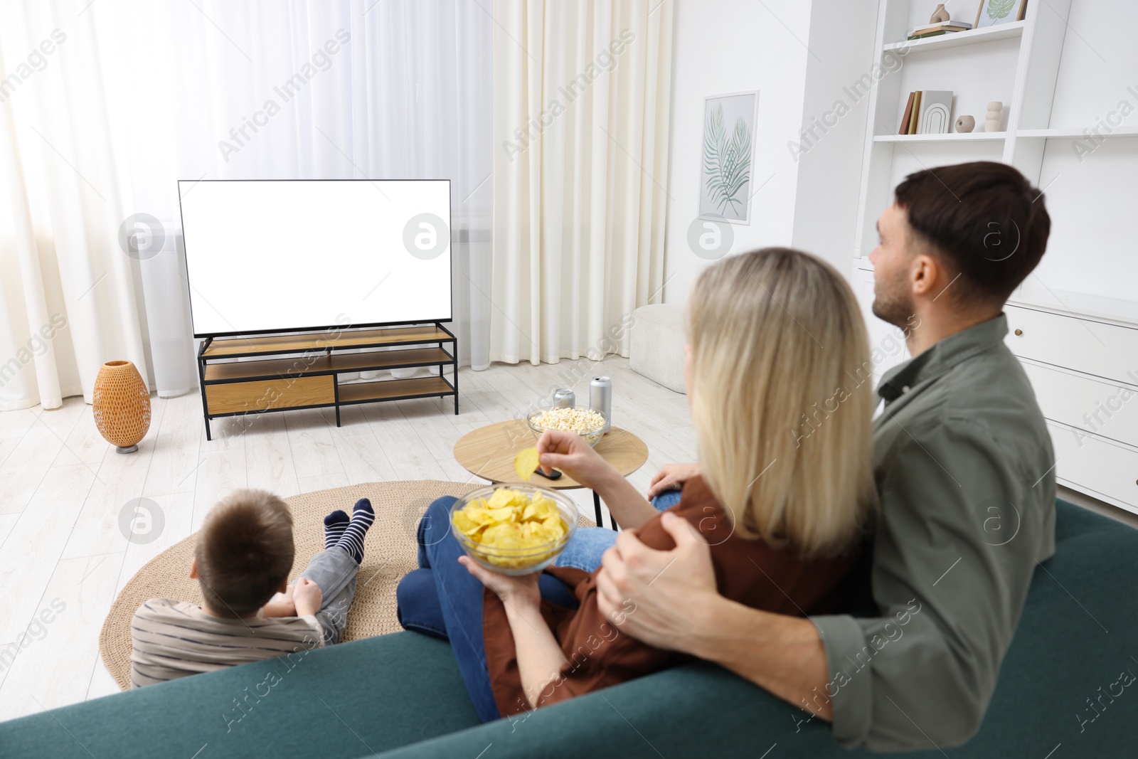 Photo of Happy family with snacks and drinks watching tv together at home