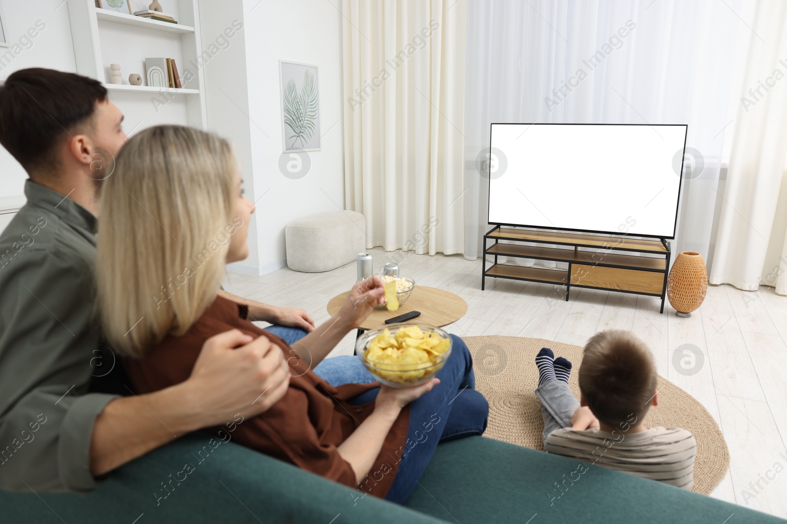 Photo of Happy family with snacks and drinks watching tv together at home