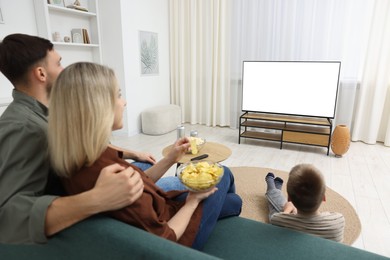 Photo of Happy family with snacks and drinks watching tv together at home