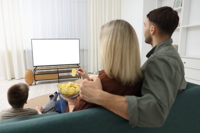 Photo of Happy family with snacks and drinks watching tv together at home