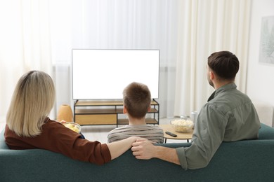 Photo of Happy family with snacks and drinks watching tv together at home, back view