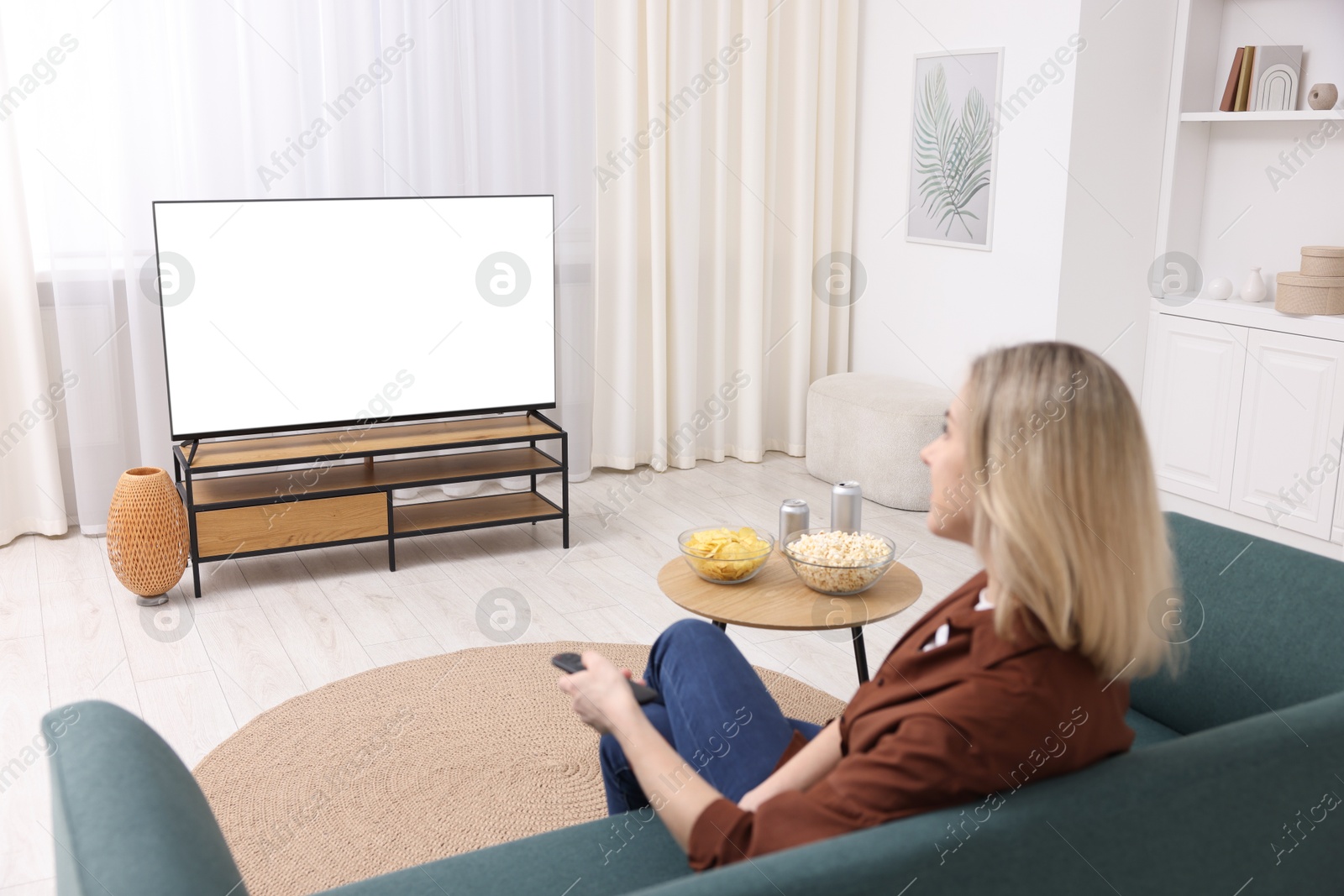 Photo of Woman with snacks and drinks watching tv on couch at home