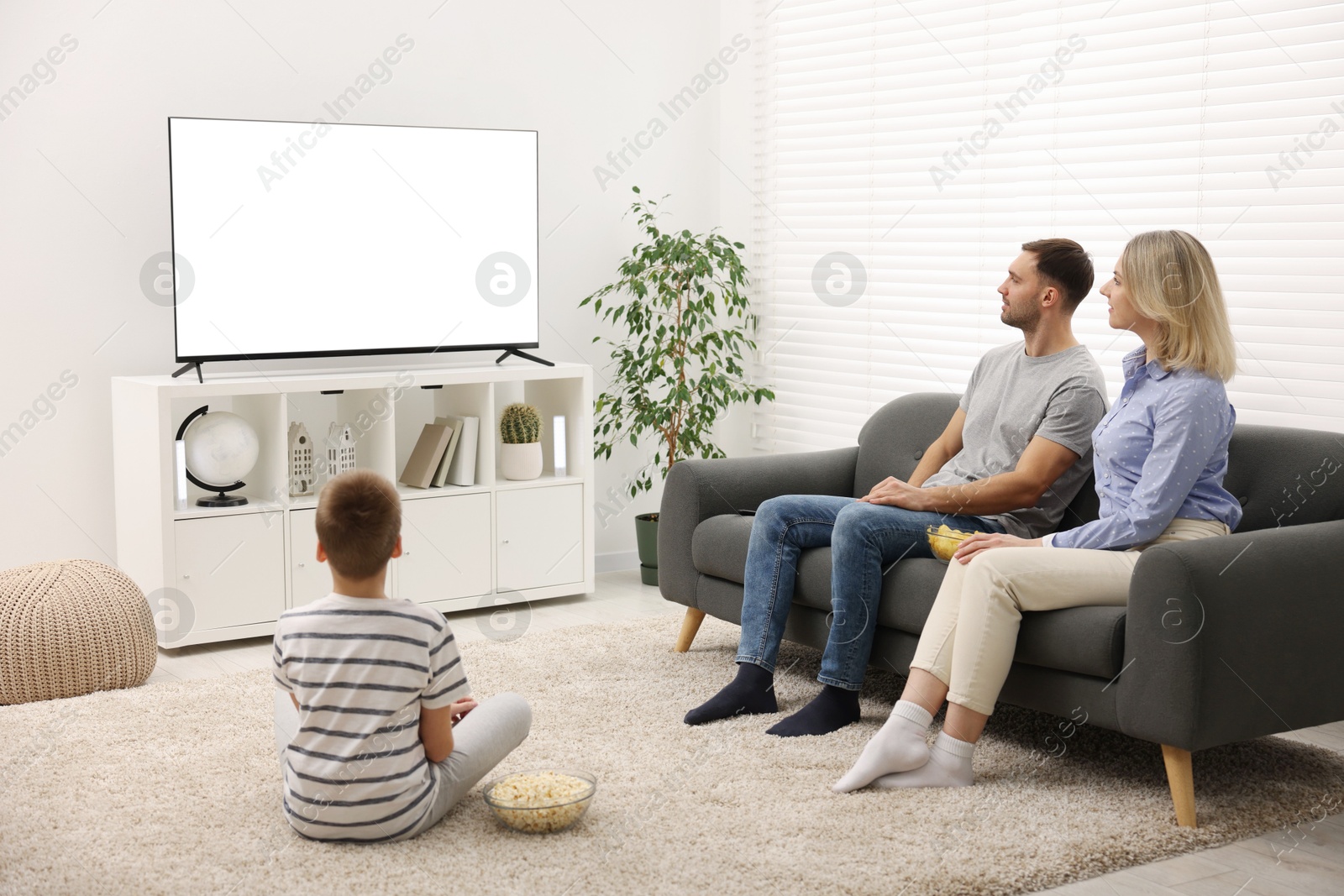 Photo of Happy family with snacks watching tv together at home