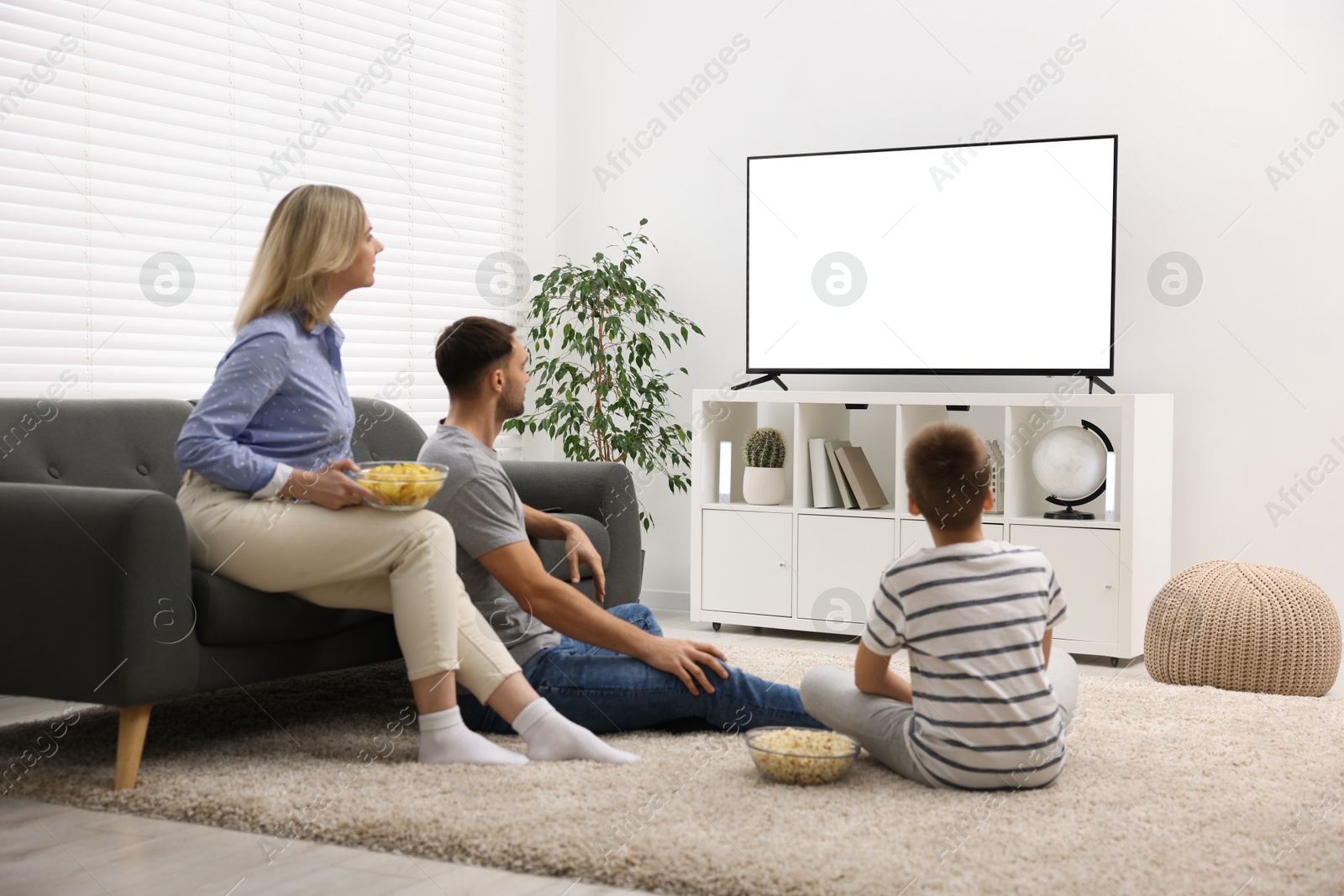 Photo of Happy family with snacks watching tv together at home