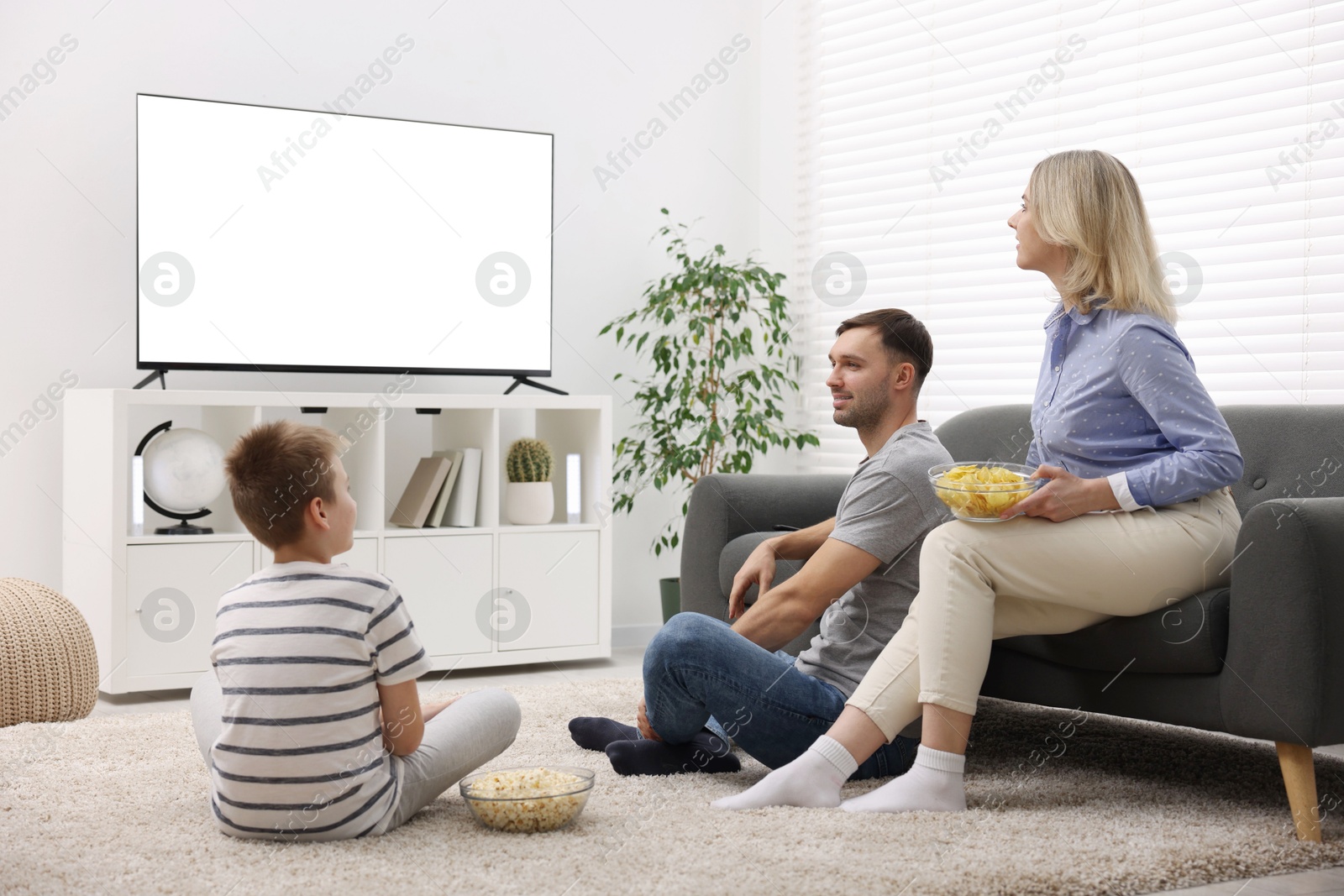 Photo of Happy family with snacks watching tv together at home