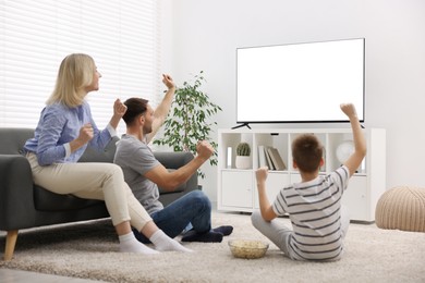 Photo of Happy family with snacks cheering while watching tv together at home