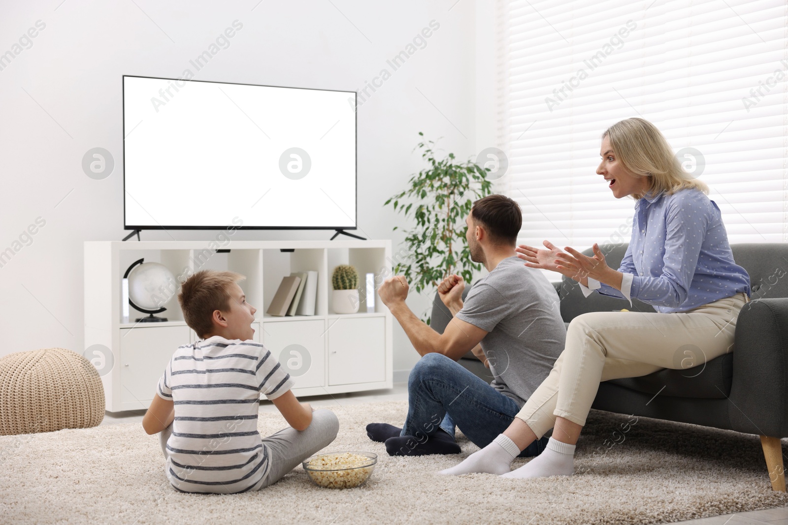 Photo of Happy family with snacks cheering while watching tv together at home