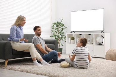 Photo of Happy family with snacks watching tv together at home