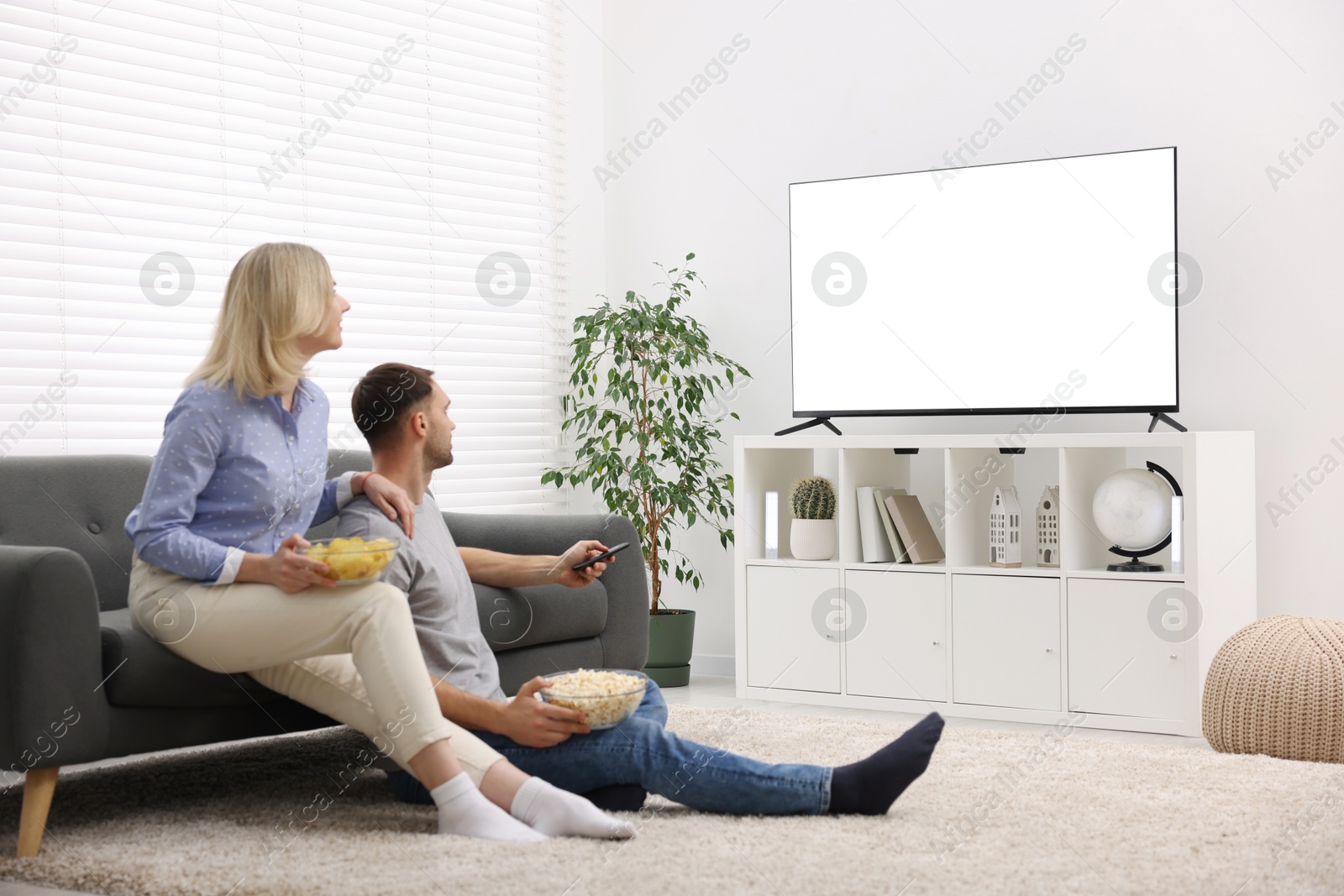 Photo of Lovely couple with snacks watching tv at home