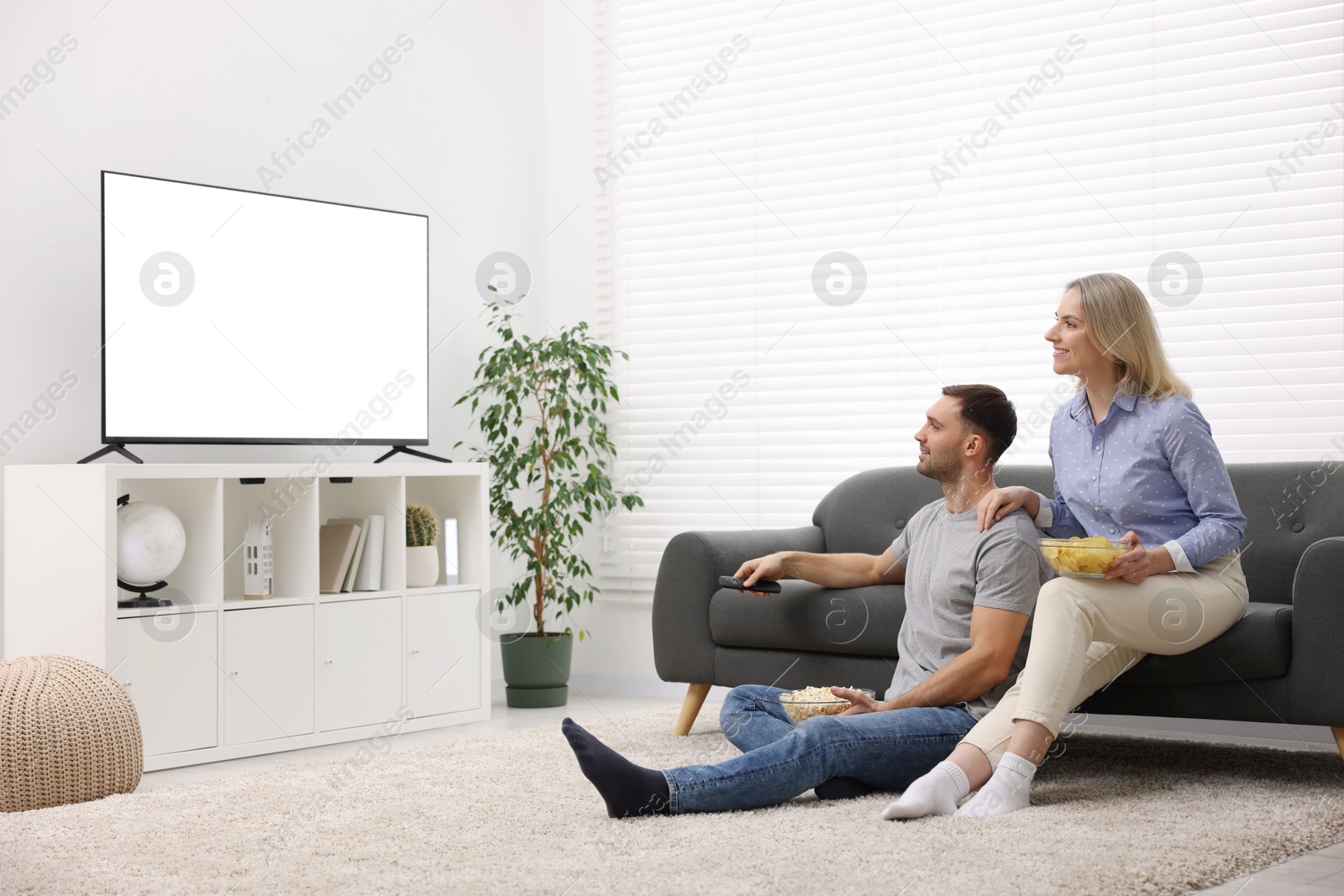 Photo of Lovely couple with snacks watching tv at home