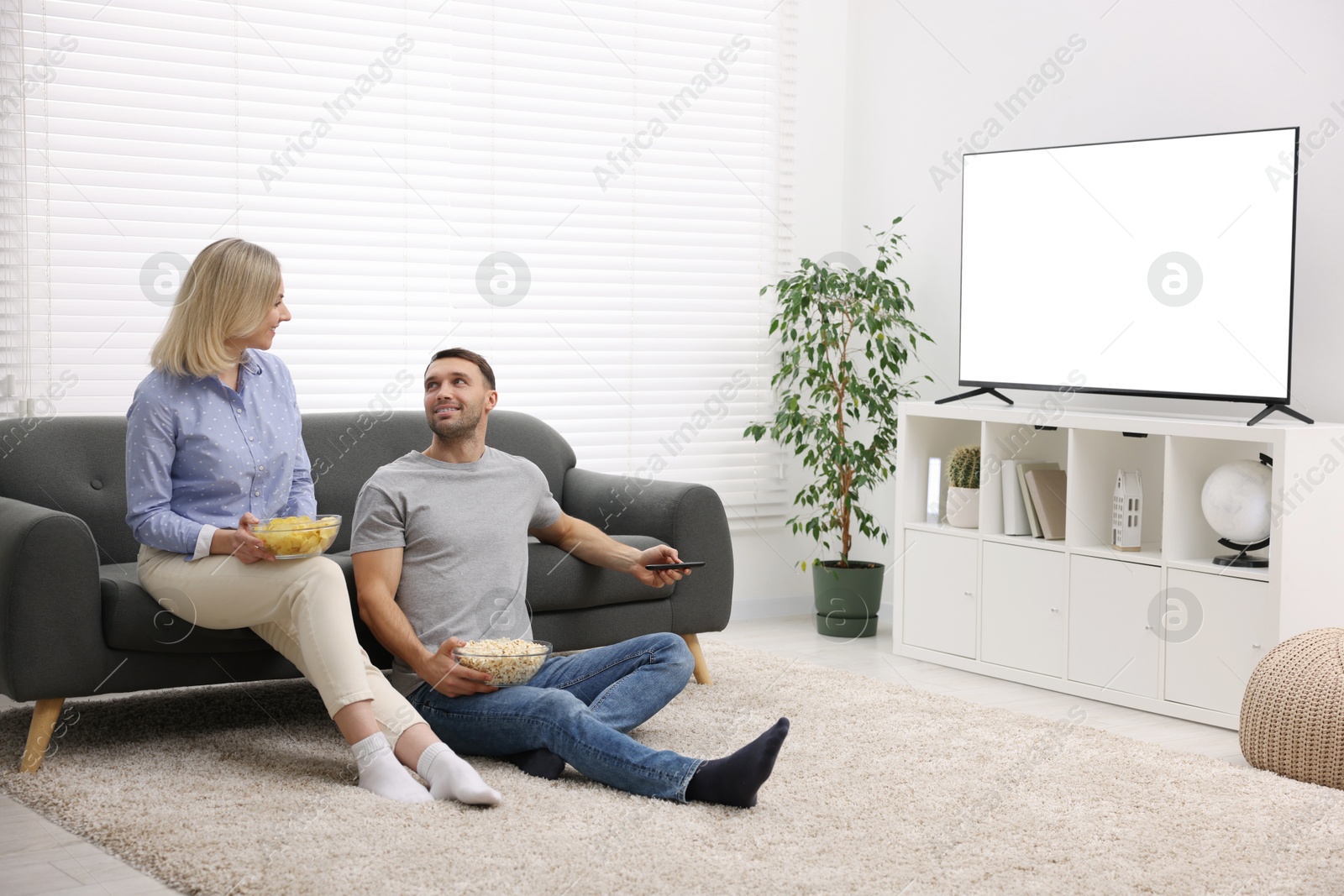 Photo of Lovely couple with snacks watching tv at home