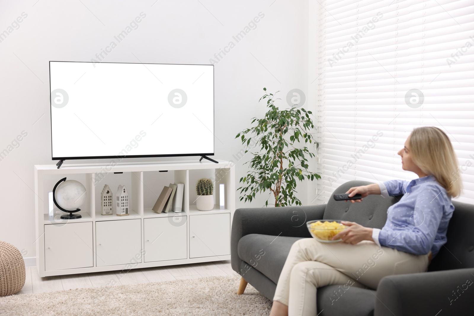 Photo of Woman with chips watching tv on couch at home