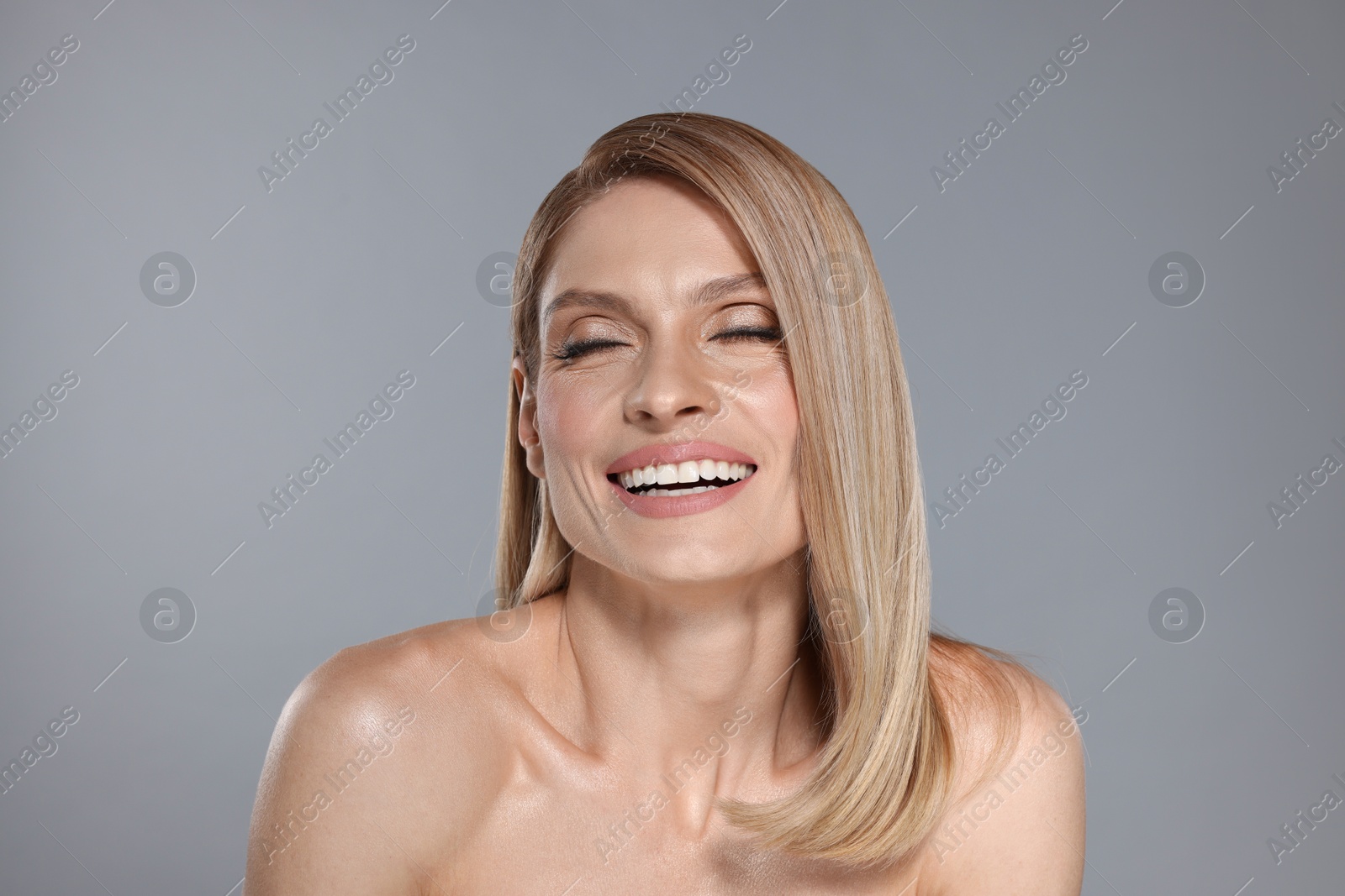 Photo of Portrait of beautiful happy woman with straight blonde hair on grey background