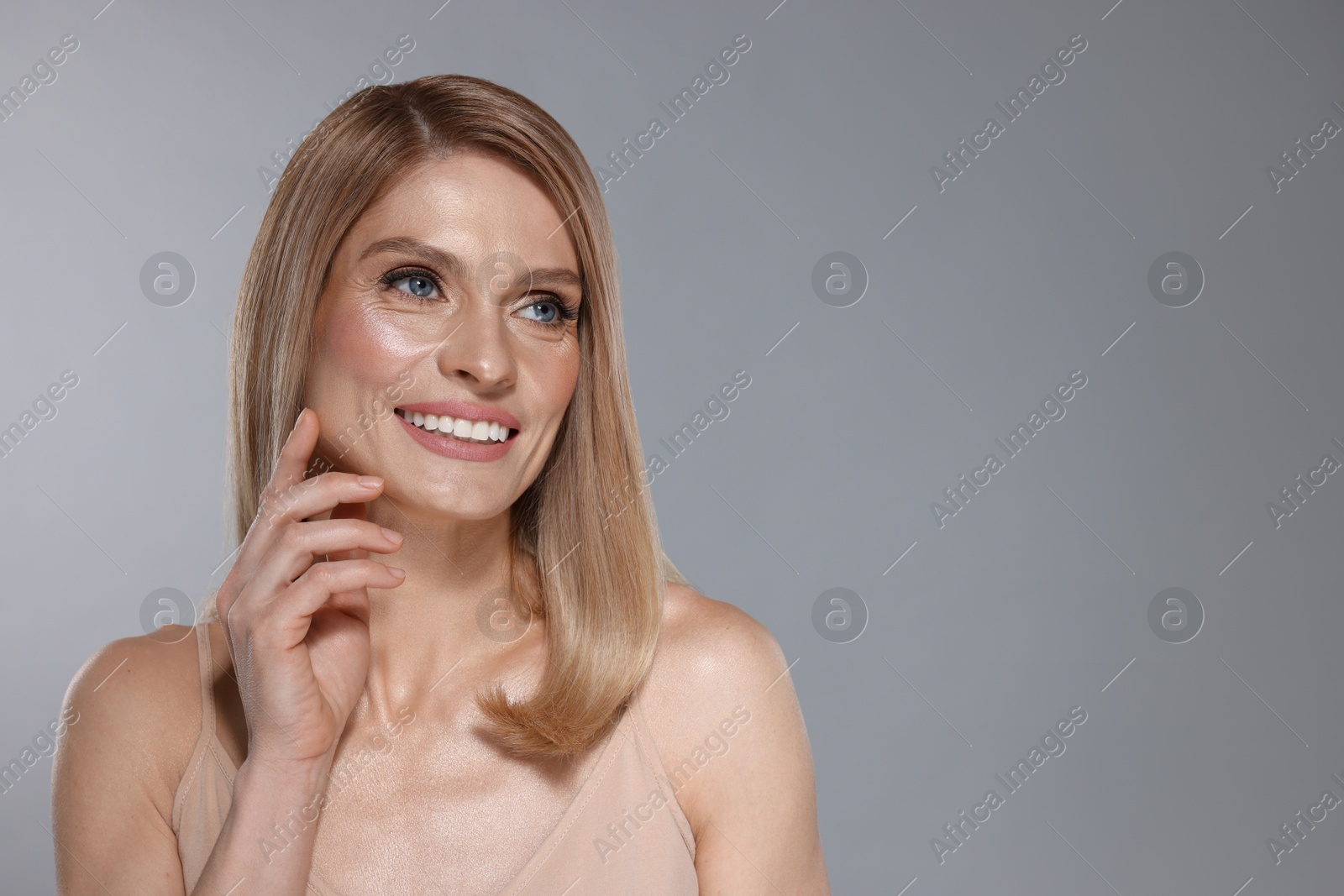 Photo of Portrait of beautiful happy woman with straight blonde hair on grey background, space for text