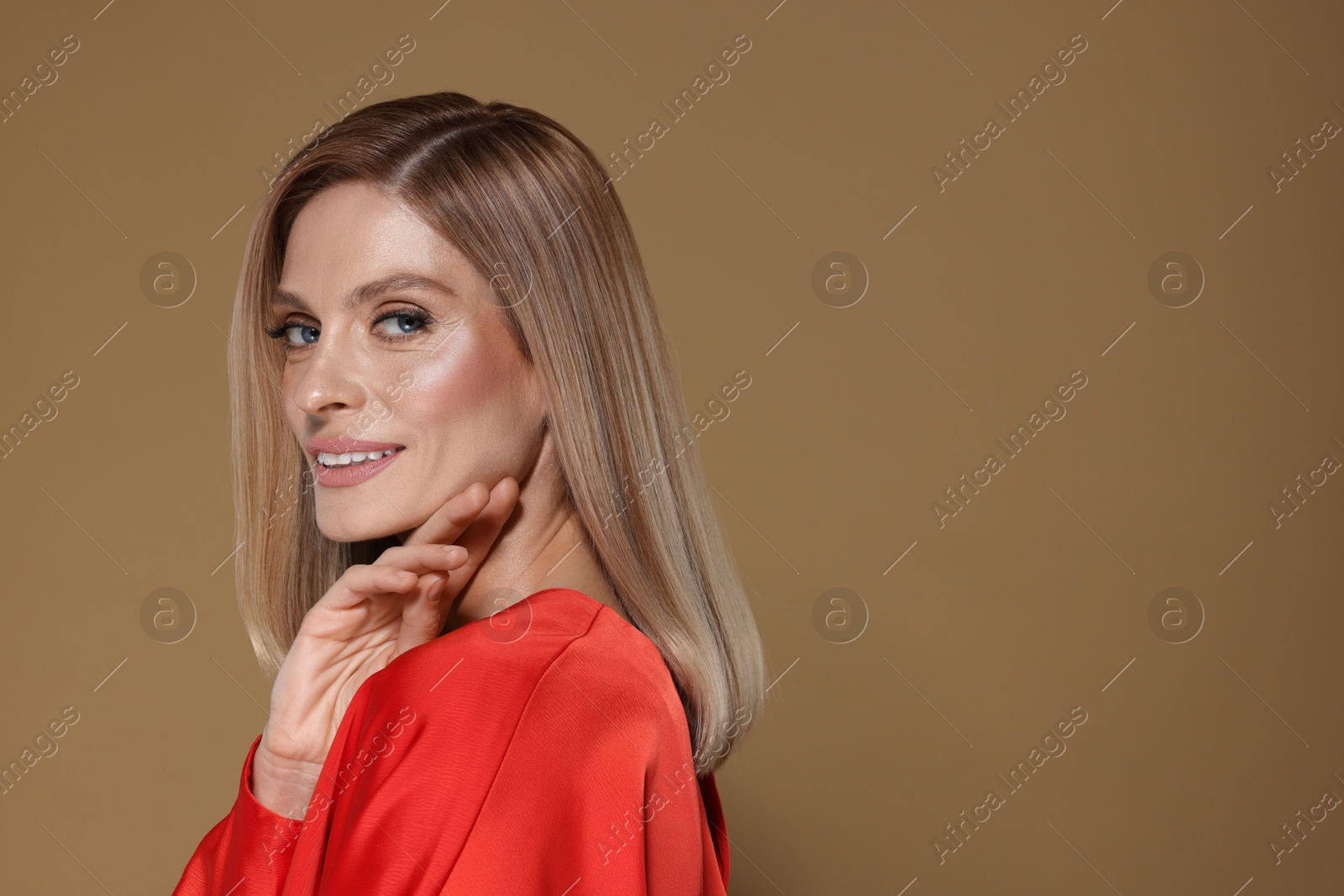 Photo of Portrait of beautiful happy woman with straight blonde hair on dark beige background, space for text