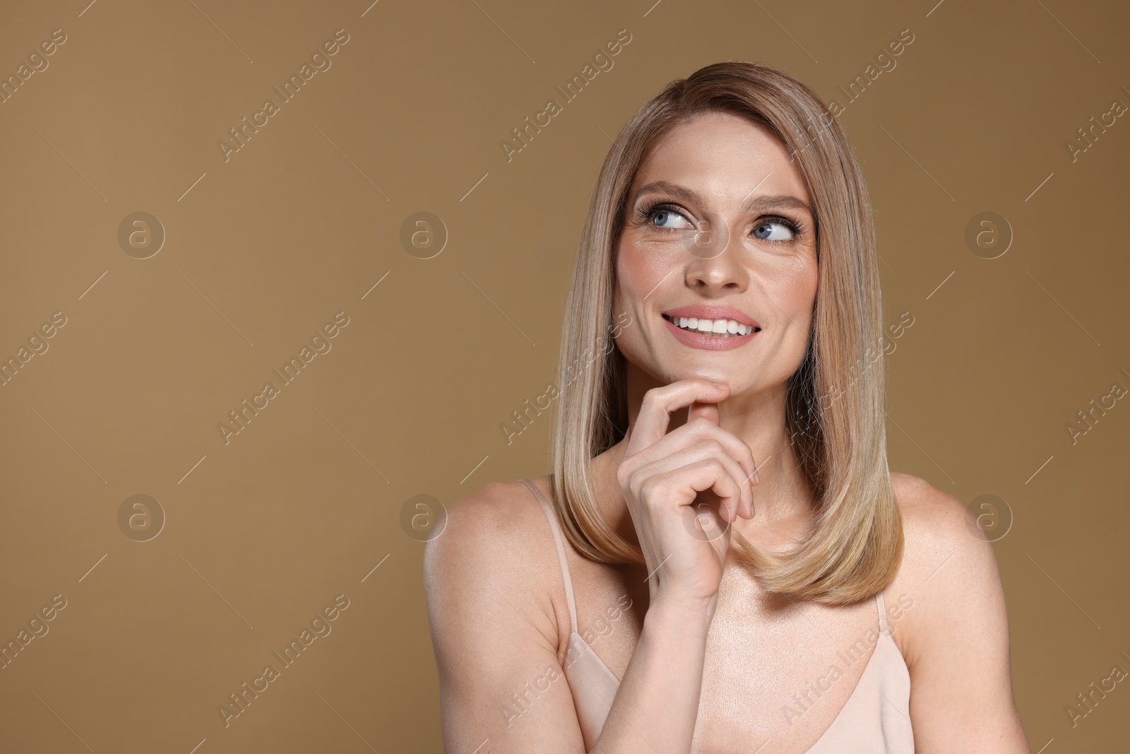 Photo of Portrait of beautiful happy woman with straight blonde hair on dark beige background, space for text