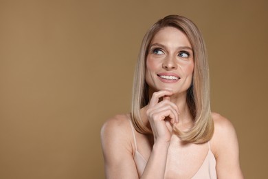 Photo of Portrait of beautiful happy woman with straight blonde hair on dark beige background, space for text