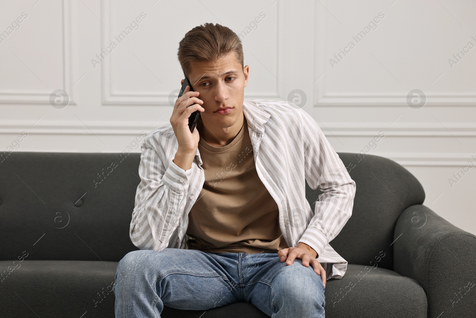 Photo of Stressed man calling hotline for mental health help on sofa at home