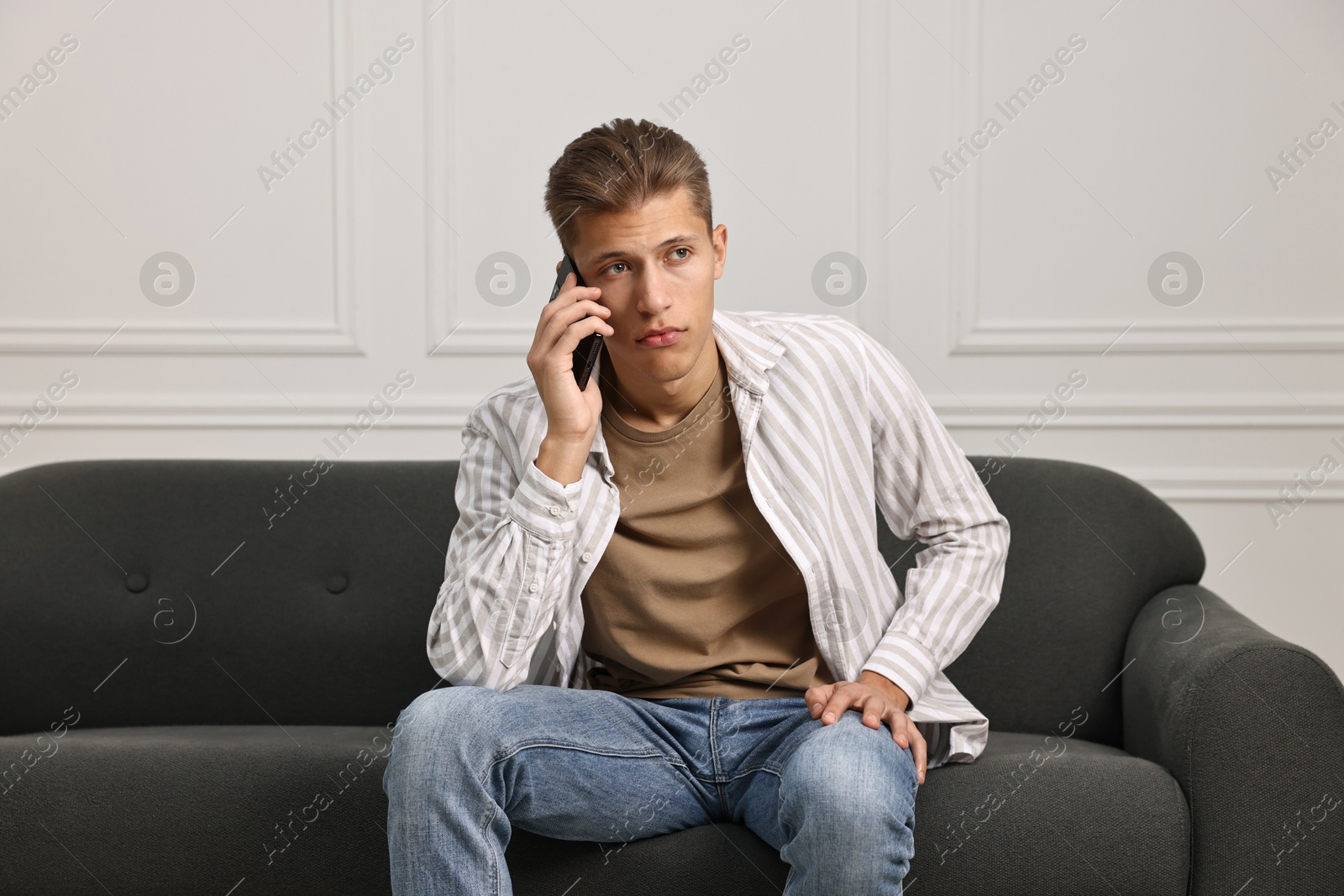 Photo of Stressed man calling hotline for mental health help on sofa at home