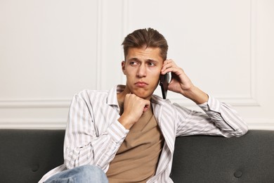 Photo of Stressed man calling hotline for mental health help on sofa at home