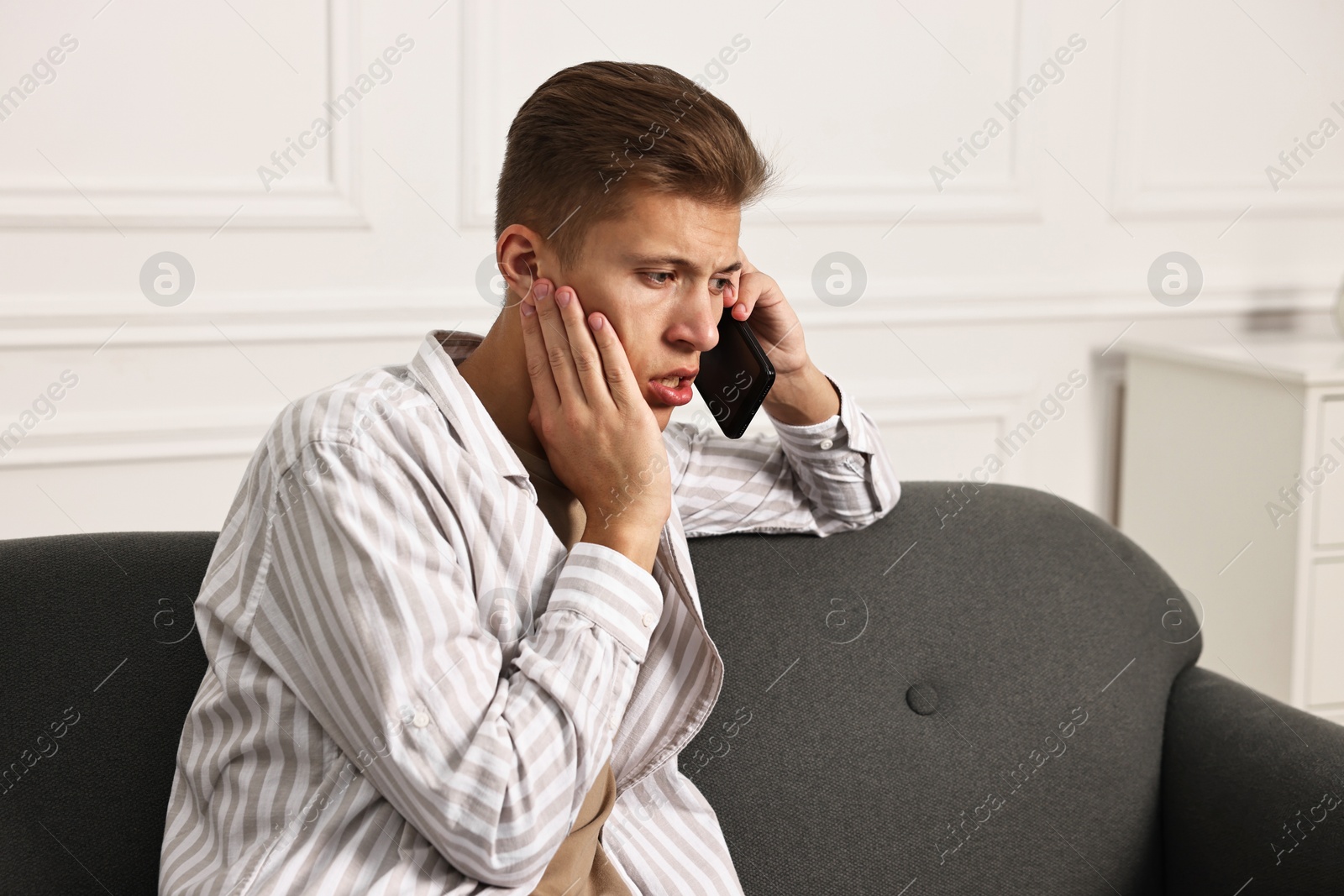 Photo of Worried man calling hotline for mental health help on sofa at home