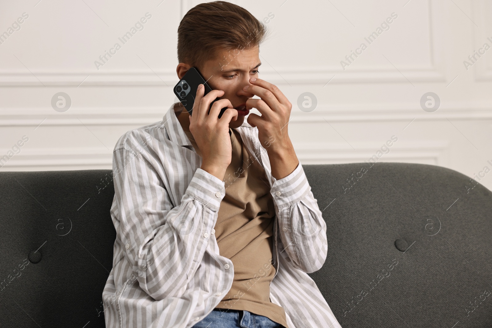 Photo of Worried man calling hotline for mental health help on sofa at home