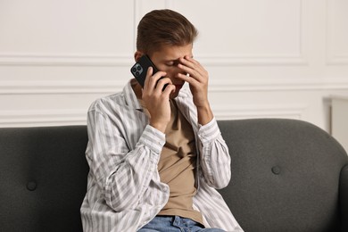 Photo of Stressed man calling hotline for mental health help on sofa at home