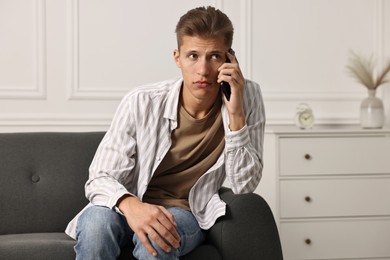 Photo of Worried man calling hotline for mental health help on sofa at home