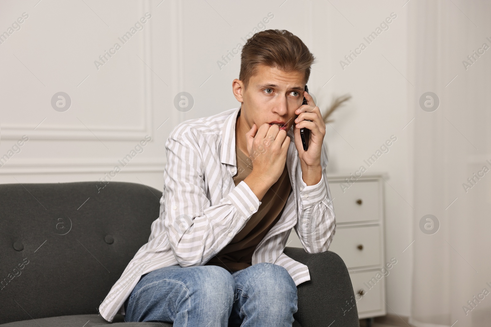 Photo of Worried man calling hotline for mental health help on sofa at home