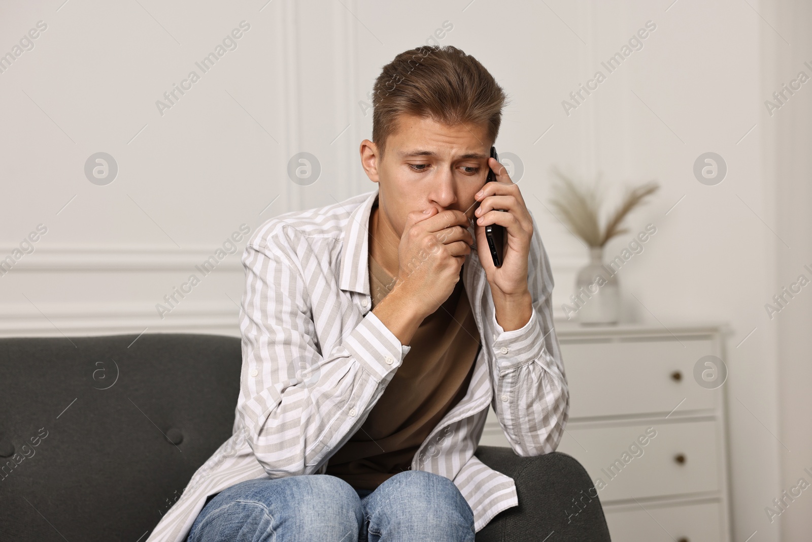 Photo of Worried man calling hotline for mental health help on sofa at home