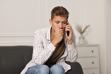 Photo of Worried man calling hotline for mental health help on sofa at home