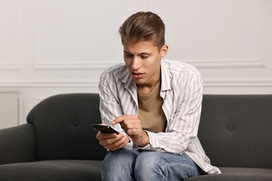 Photo of Worried man calling hotline for mental health help on sofa at home