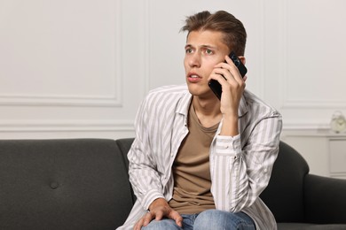 Photo of Worried man calling hotline for mental health help on sofa at home. Space for text