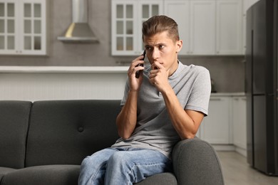 Photo of Stressed man calling hotline for mental health help on sofa in kitchen