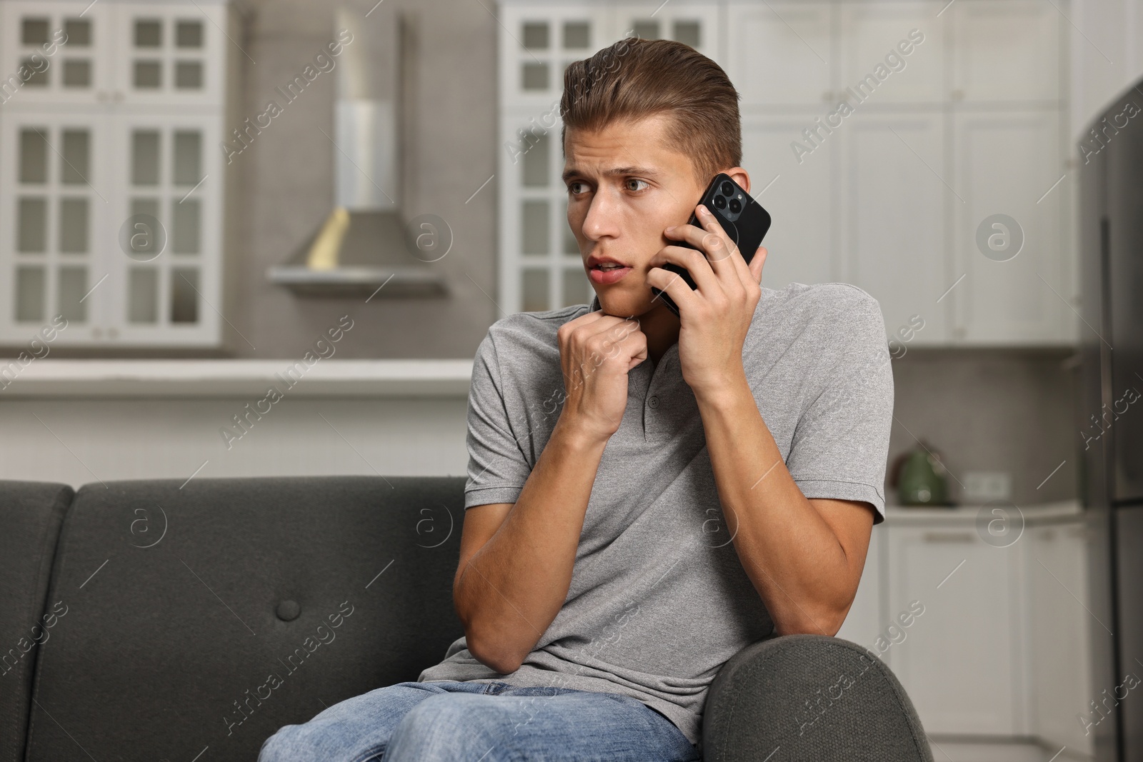 Photo of Stressed man calling hotline for mental health help on sofa in kitchen