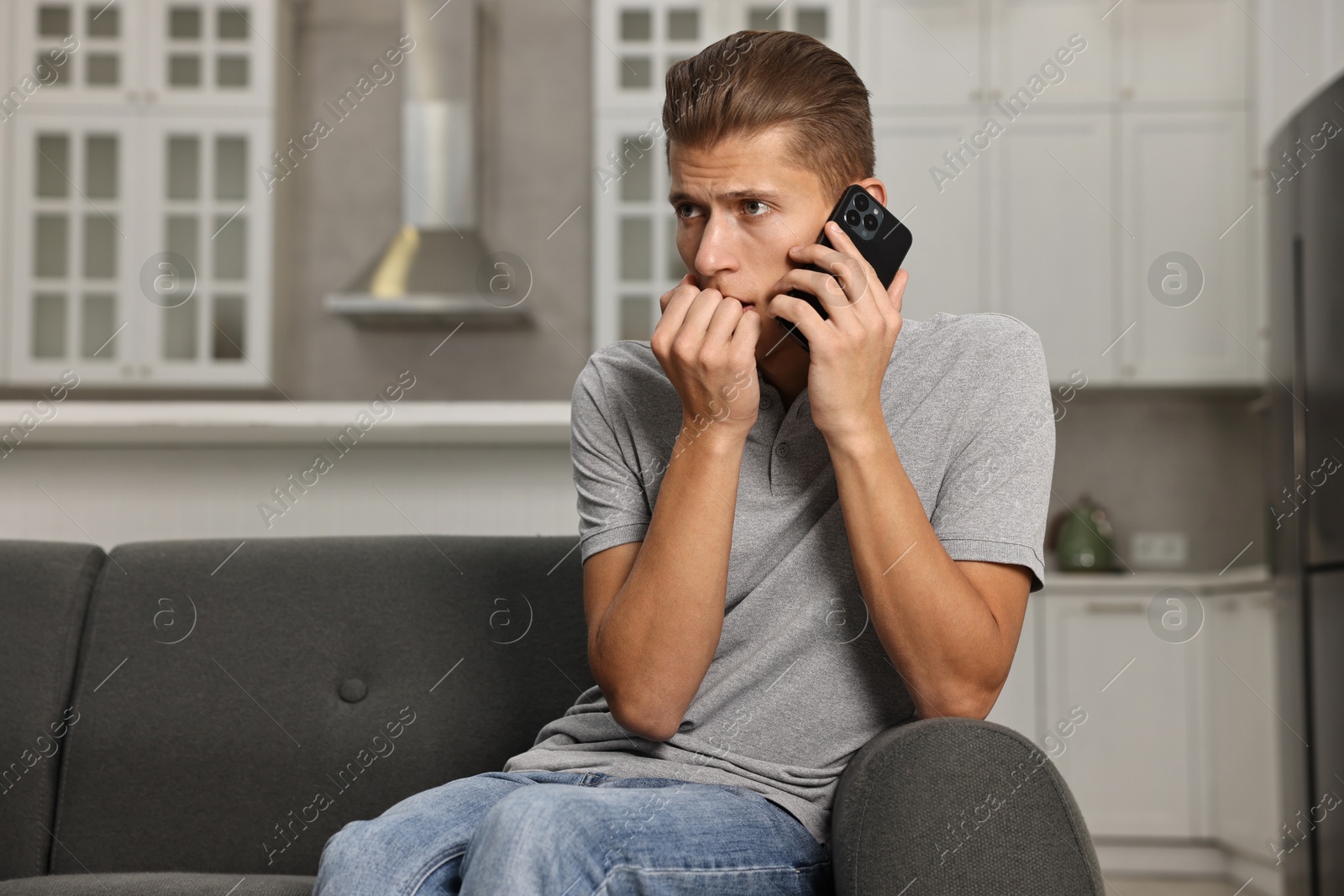 Photo of Stressed man calling hotline for mental health help on sofa in kitchen