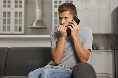 Photo of Stressed man calling hotline for mental health help on sofa in kitchen