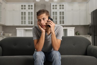 Photo of Stressed man calling hotline for mental health help on sofa in kitchen