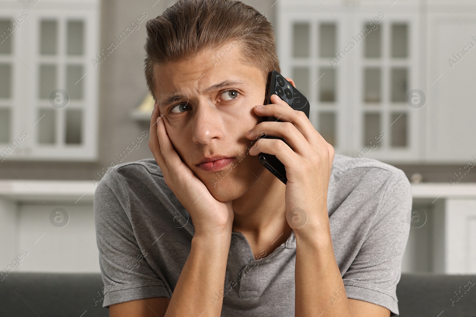 Photo of Stressed man calling hotline for mental health help on sofa in kitchen