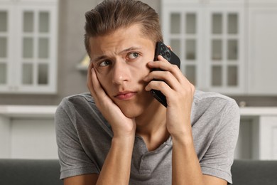 Photo of Stressed man calling hotline for mental health help on sofa in kitchen