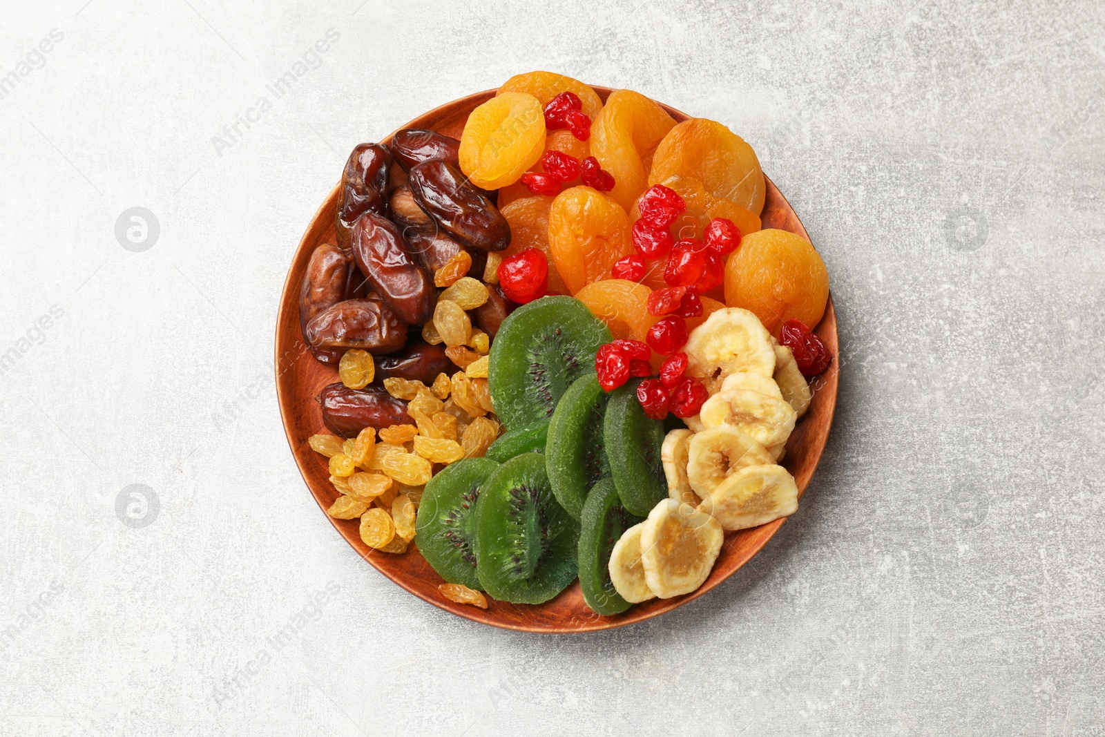 Photo of Mix of different dried fruits in bowl on light grey table, top view