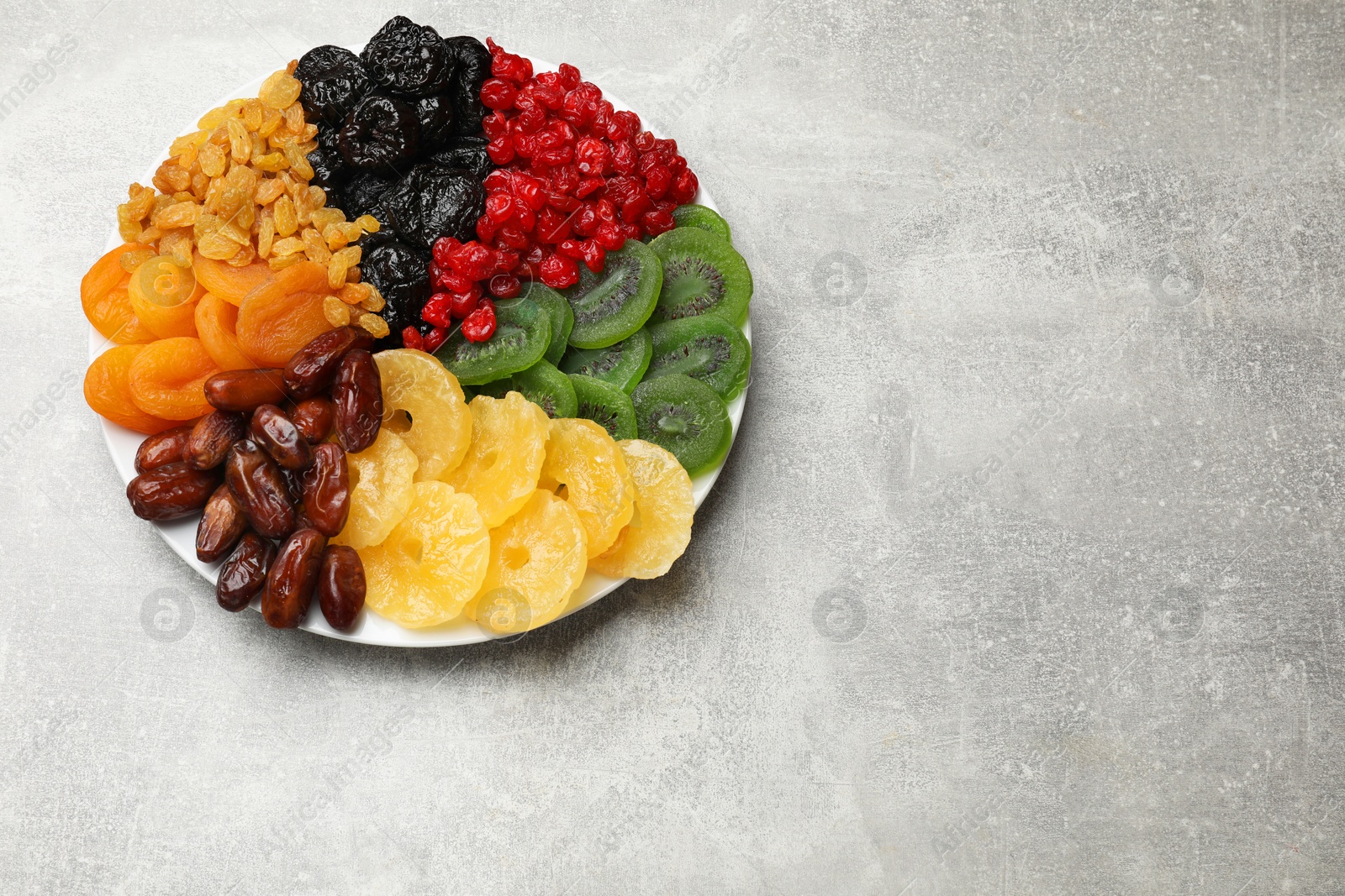 Photo of Mix of different dried fruits on gray textured table, top view. Space for text