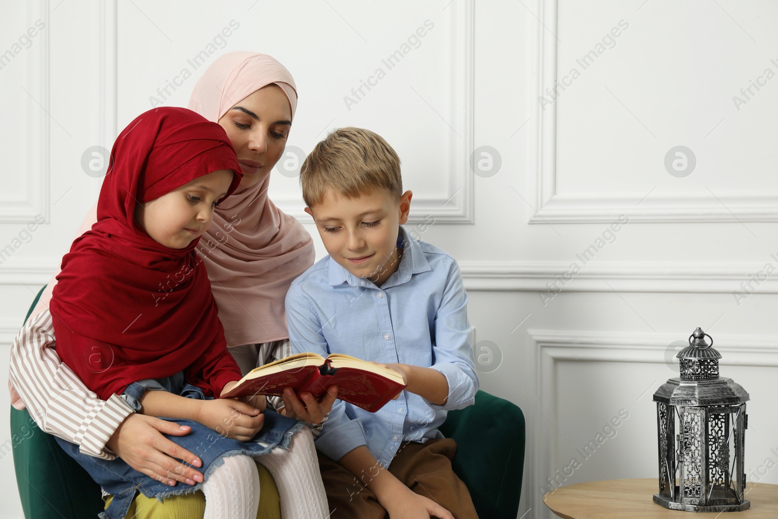 Photo of Muslim woman and her children reading Quran at home